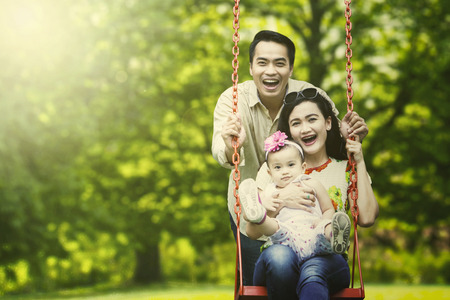 Image of happy parents playing swing with their daughter in the parkの写真素材