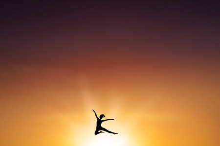 Silhouette of carefree young woman enjoy life and leaps on the air at dusk timeの写真素材