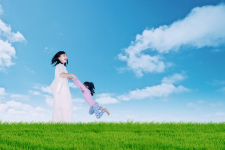 Joyful young woman spinning her daughter on the meadow, shot at summertimeの写真素材