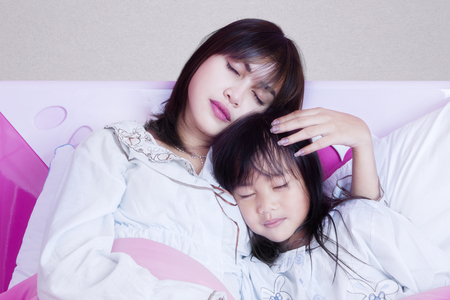 Portrait of a beautiful young mother and her daughter sleeping together on the bedroom at homeの写真素材