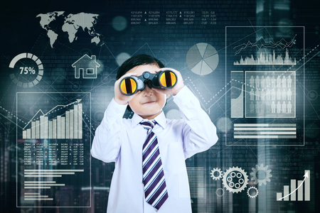 Image of a little businessman using a binocular while looking at the camera and standing with growth business in the backgroundの写真素材