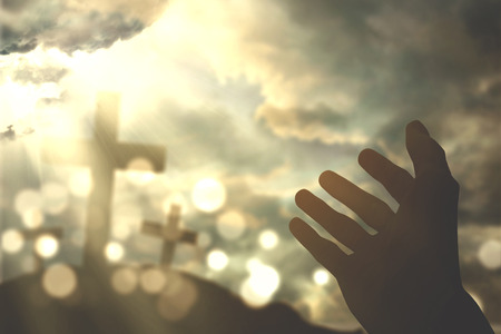 Picture of human hands praying to the GOD with christian cross symbol and bright sunlight on the skyの写真素材