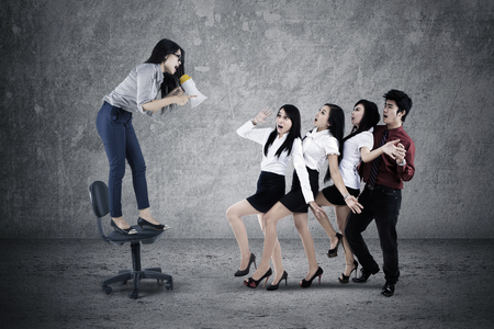 Picture of female leader shouting with a megaphone to her teamwork while standing on the chairの写真素材