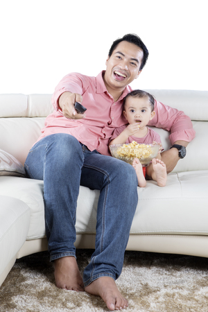 Image of Asian father and daughter watching tv together while eating popcorn in the studioの写真素材