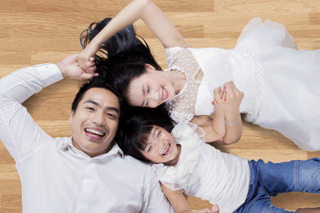 High angle view of attractive Asian family lying on the wooden floor while smiling and holding hands togetherの写真素材