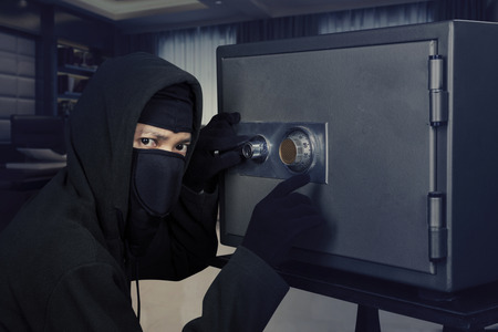 Picture of a male burglar wearing a mask and trying to steal a safe deposit box in the office