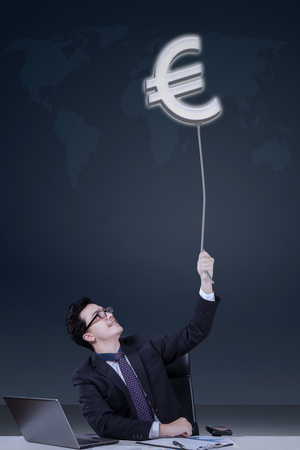 Male manager working with laptop on desk and pulling an euro currency symbolの写真素材