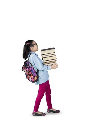 Image of little girl carrying pile of books while walking in the studio, isolated on white backgroundの写真素材