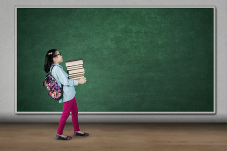 Picture of cute student carrying pile of books while walking in the classroomの写真素材