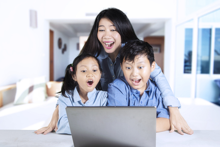 Photo of two shocked children and her mother, looking at a laptop screen. Shot at homeの写真素材