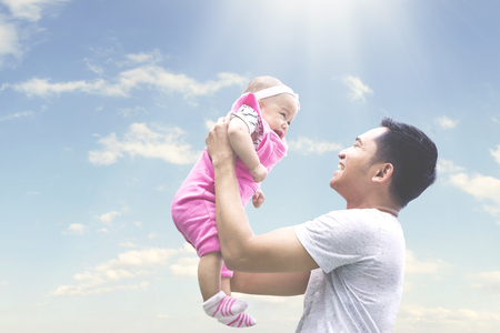 Photo of a young happy father holding his baby under sunny day, shot outdoorsの写真素材