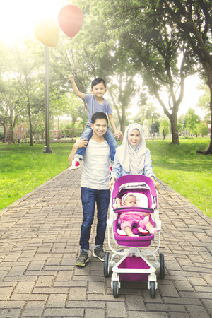 Portrait of beautiful muslim family walking in the park with baby on the stroller and the son holding balloonsの写真素材