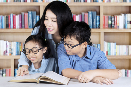 Picture of pretty female teacher helping her students to read a book while sitting in the libraryの写真素材