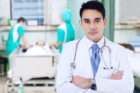 Portrait of handsome doctor wearing uniform, looks confident while standing in patient roomの写真素材