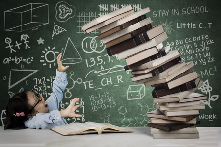 Picture of cute schoolgirl holds a pile of falling books with doodles on the chalkboardの写真素材