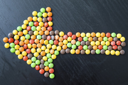 Top view of arrow sign made of sweet colorful candy on the table