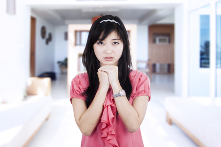 Picture of a worried young woman standing in the living room at homeの写真素材