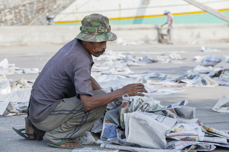 JAKARTA, Indonesia. April 20, 2017: Old man taking up garbage of paper in the dirty harborのeditorial素材