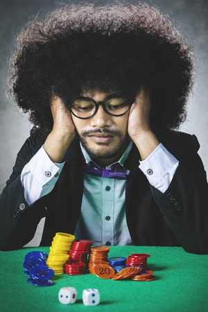 Picture of Sad Afro man looking at chips and dice on the table after lose in gamblingの写真素材