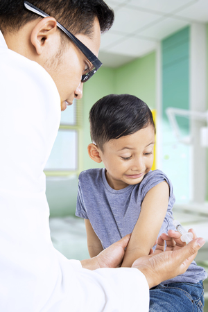 Male pediatrician using a syringe for giving vaccine to his patient in the hospital roomの写真素材
