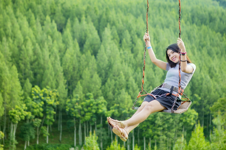 Photo of Asian young woman playing on a swing with pine forest backgroundの写真素材