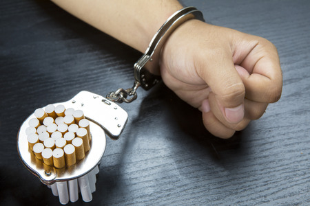 Arm of man and cigarettes is bonding with a handcuffs on the wooden tableの写真素材