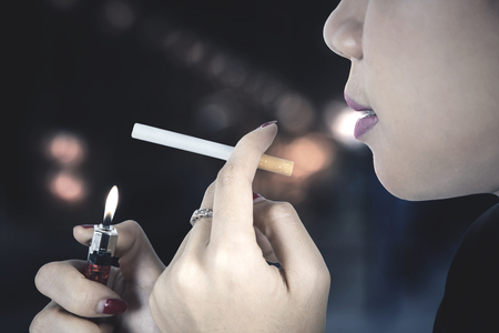Close up of female smoker burning her cigarette with a lighter, shot with blur backgroundの写真素材