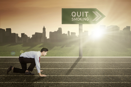 Image of Middle Eastern businessman ready to run with text of quit smoking on the signpostの写真素材