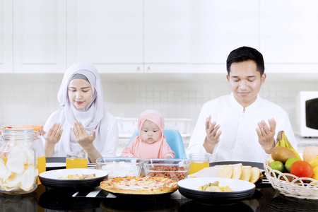 Portrait of young parents and cute girl praying together in dining table while sitting in the kitchenの写真素材