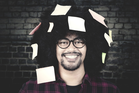 Young Afro man smiling at the camera with   notes attached on his curly hair