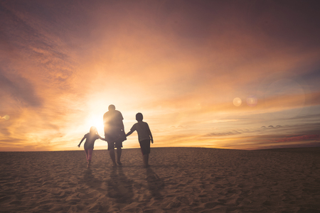 Rear view of father and children walking together on the sand at sunset timeの写真素材