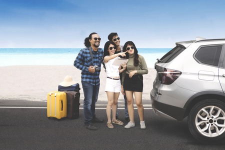 Multiracial group of young people standing near the beach while looking something with digital...