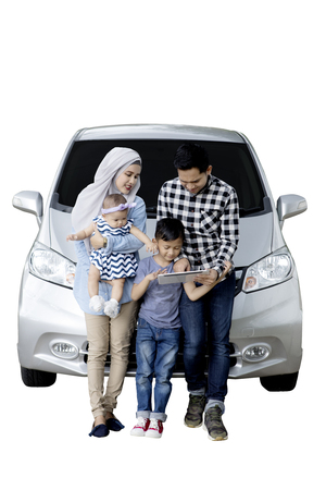Portrait of Muslim family using a digital tablet while sitting on the hood of their car, isolated on white backgroundの写真素材