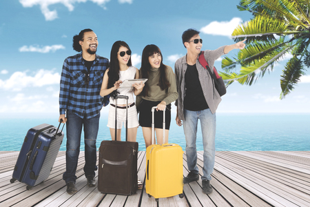 Group of happy multi ethnic friends standing on the wooden pier with their luggage and looking at somethingの写真素材