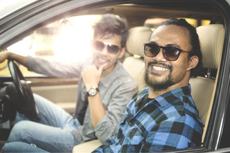 Two young men wearing sunglasses, sitting in the car while smiling at the cameraの写真素材
