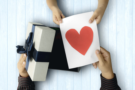 Top view of an Asian father holding a gift card with heart symbol while opening a present from his...