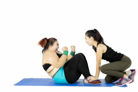 Obese woman doing sit up on the mat helped by her instructor, isolated on white backgroundの写真素材