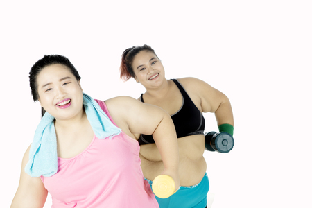 Two women doing workout while holding dumbbell, isolated on white backgroundの写真素材