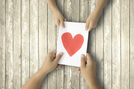 Father's Day. Hands of father and child holding a greeting card with love symbol on the wooden tableの写真素材