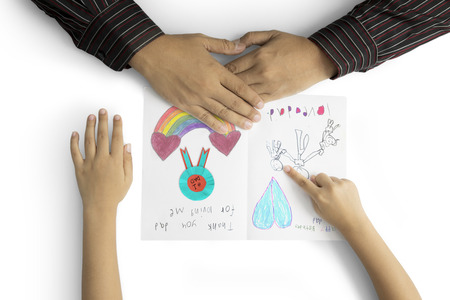Father's Day. Hands of little child showing a greeting card to his father with heart symbol, handwritten, and family pictureの写真素材