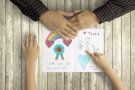 Close up of little child showing hand painting to her father on greeting card with wooden backgroundの写真素材