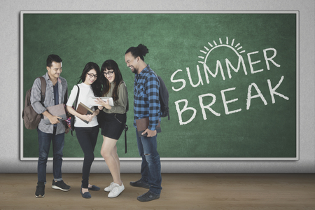 Diversity students using a digital tablet together while standing with text of summer break at the blackboardの写真素材