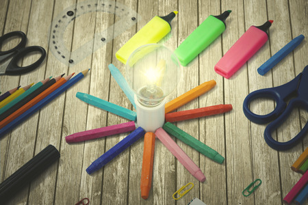 Closeup of a bright bulb with multicolored school supplies on the wooden tableの写真素材