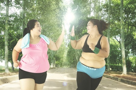 Two overweight women running on the park while giving high five together, shot outdoorsの写真素材