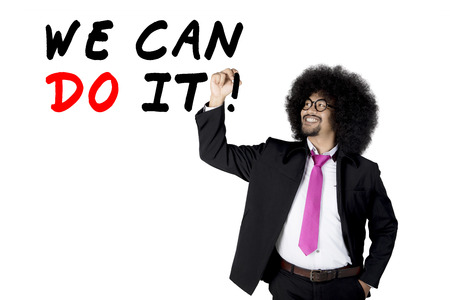 Young Afro businessman writes a text of We Can Do It on the whiteboard, isolated on white backgroundの写真素材