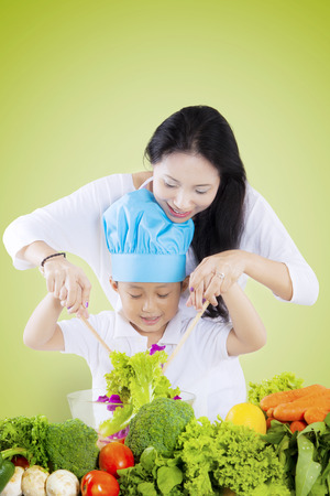 Young Asian mother helping her son make a bowl of vegetables salad, shot with green screen backgroundの写真素材