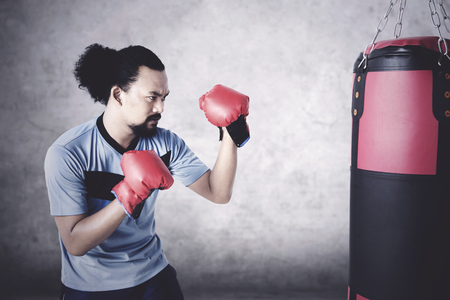 Young Afro man practice boxing while wearing gloves and punching a sackの写真素材