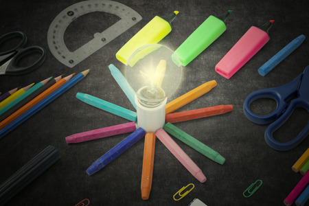 Closeup of a bright bulb with colored crayons and school supplies on the blackboardの写真素材