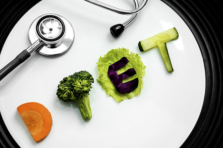 Close up of slices healthy vegetable salad shaped diet word with a stethoscope on the plate