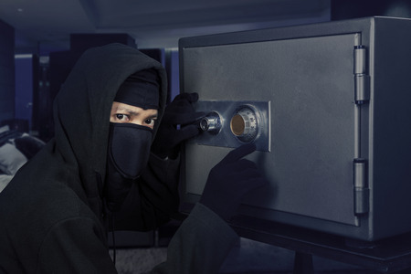 Male burglar wearing a mask and trying to steal a bank vault in the bedroom at homeの写真素材